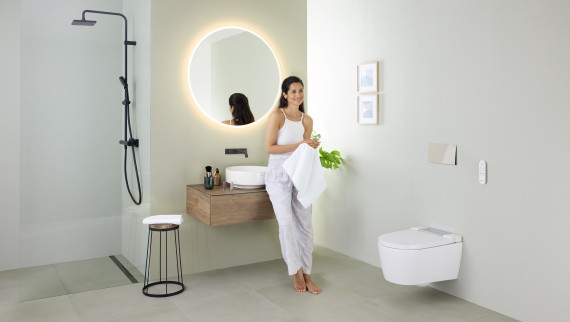 Kobieta opierająca się o umywalkę w łazience z toaletą myjącą Geberit AquaClean Sela oraz umywalką i meblami z serii Geberit VariForm