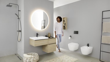 Mężczyzna wchodzi do łazienki z umywalką, WC, bidetem i meblami łazienkowymi z serii Geberit iCon.