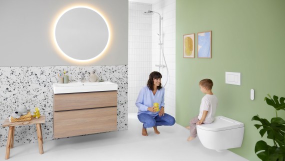 Kobieta i dziecko w kolorowej łazience z lustrem Geberit Option i toaletą myjącą Geberit AquaClean Alba