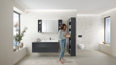 Kobieta otwiera wysoką szafkę z dużą ilością miejsca do przechowywania w łazience z meblami łazienkowymi z serii Geberit Acanto
